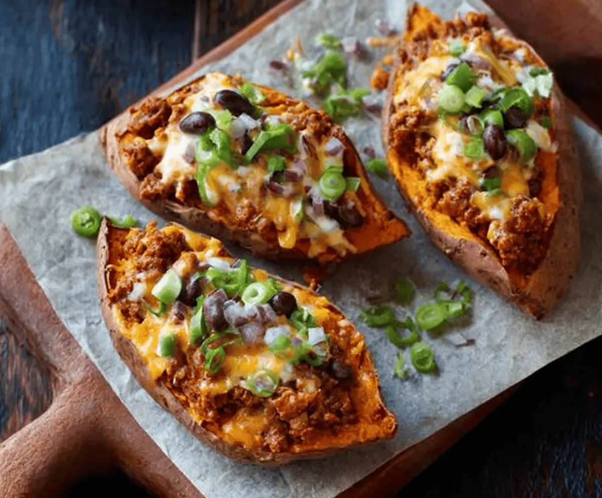 Creamy cheesy chili stuffed sweet potatoes topped with melted cheese and fresh herbs, perfect for a hearty and flavorful meal.