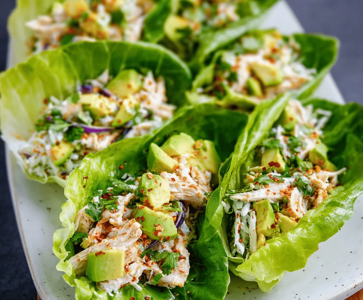 Fresh avocado chicken lettuce wraps served on a white plate, featuring diced chicken, ripe avocado slices, and crisp lettuce leaves, perfect for a healthy, low-carb meal.