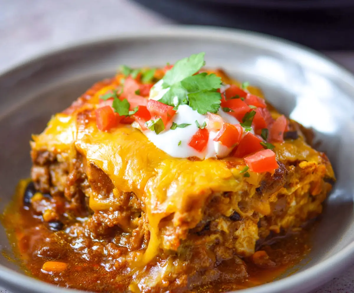 Delicious Crockpot Beef Enchilada Casserole in a baking dish, topped with melted cheese and garnished with fresh herbs.