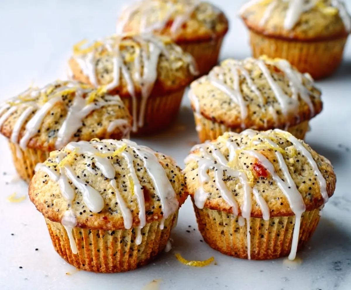 Freshly baked Zesty Glazed Lemon Poppy Seed Muffins topped with lemon glaze and poppy seeds.